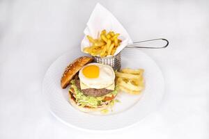 beef burger with sunny side up egg and french fries bucket served in dish isolated on table top view of arabic food photo