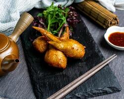 Mentaiko Chicken Wings with chili sauce green leaves and chopsticks isolated on cutting board side view of appetizer japanese fastfood on table photo