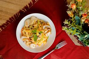 tropical pasta ensalada con mezcla carne aceituna con camarón y gamba servido en cuenco con flores y tenedor aislado en rojo servilleta lado ver de sano verde comida en mesa foto