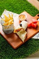 Chipotle Chicken Egg wrap roll filled with tomato, onion, cucumber, cheese with french fries, mayo dip and watermelon slice served on wooden board top view of fastfood appetizer photo