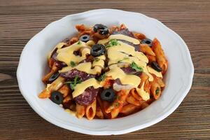 Salami and cheese pasta with black olive and tomato sauce served in dish isolated on table side view of arabic food photo