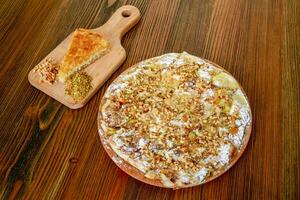 Kunafa with nuts pie walnut, almond and pistachio served in wooden board isolated on table side view of arabic food photo