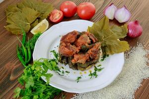 vine leaves meat casserole with tomato, onion, rice, coriander, lemon slice and green chilli served in dish isolated on wooden table side view of arabic food photo