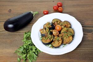 Marinated fried eggplant with cherry tomato and coriander served in dish isolated on wooden table side view of arabic food photo