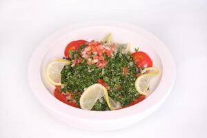 TABOULEH Salad eith tomato, leaves, and lemon slice served in dish isolated on background side view of arab food photo