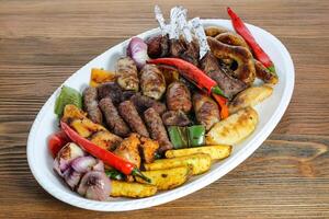 Mix grill family platter tikka kabab, lamb chop, meat kebab, chicken, beef, mutton, potato veggies, tomato and onion served in dish isolated on table side view of arabic food photo