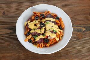 Salami and cheese pasta with black olive and tomato sauce served in dish isolated on table top view of arabic food photo