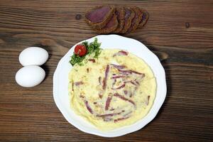 Pastrami omelette with smoked meat served in dish isolated on wooden table top view of arabic food photo