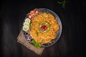 vegetable chow mein with capsicum, tomato, cucumber, onion and chilli sauce served in dish isolated on napkin dark background top view of indian fastfood photo