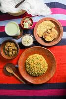 Achari Chicken Khichuri Combo with egg plant and omelet, borhani, salad and Chui Pitha served in dish isolated on mat top view of indian and bangladeshi food photo