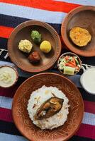 Khuder Bhat, Hilsa Khichuri Combo with salad, eggplant, borhani and Chui Pitha served in dish isolated on mat top view of indian and bangladeshi food photo