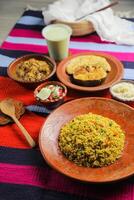achari pollo kichuri combo con huevo planta y tortilla, borhani, ensalada y Chui pitha servido en plato aislado en estera parte superior ver de indio y bangladeshi comida foto