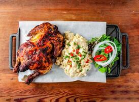 Whole grilled chicken with side dishes mac and cheese served on board isolated on wooden table top view of hong kong food photo