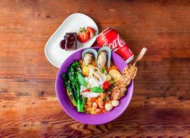 seafood laksa soup with shrimp, prawn, sea shell, noodles and boiled egg with skewer, chicken satay, brownie and coke can 330 ml served in dish isolated on wooden table top view of hong kong food photo