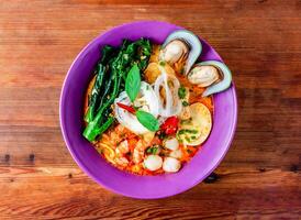 seafood laksa soup with shrimp, prawn, sea shell, noodles and boiled egg served in dish isolated on wooden table top view of hong kong food photo