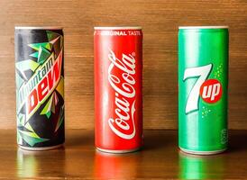 Assorted soft drink cans with coke, 7up and dew isolated on wooden background side view of indian spices and pakistani food photo