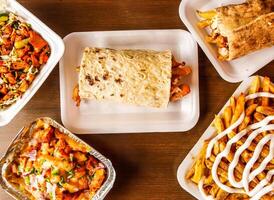 afghani sausage shawarma, chicken wrap, pizza loaded fries, mayo fries or potato chips and chicken diet salad served in dish isolated on wooden background top view of indian spices and pakistani food photo