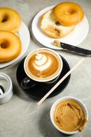 caliente caramelo de azúcar con mantequilla latté Arte café servido en taza con llanura donas, azúcar y cuchillo aislado en servilleta lado ver café desayuno foto