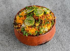 picante niño, matka o arcilla pollo Biryani maceta Adición con Lima rebanada y oriandro servido en plato aislado en gris antecedentes lado ver de indio especias y pakistaní comida foto