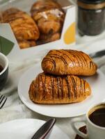 Chocolate Croissant served on plate with cup of black coffee with knife and fork isolated on napkin side view of french breakfast baked food item on grey background photo