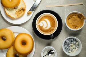 caliente caramelo de azúcar con mantequilla latté Arte café servido en taza con llanura donas, azúcar y cuchillo aislado en servilleta parte superior ver café desayuno foto