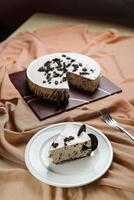 Oreo Cheesecake slice include chocolate, cream, sugar with fork and flowers served in plate isolated on napkin side view of cafe food photo