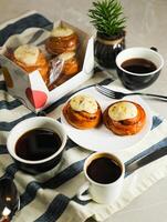 Cinnamon Roll served in plate with cup of black coffee with knife and fork isolated on napkin side view of french breakfast baked food item photo