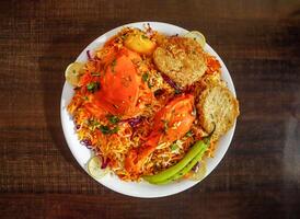 Spicy chicken biryani with shami kabab, potato, and lemon slice served in plate isolated wooden background top view indian spices and pakistani food photo