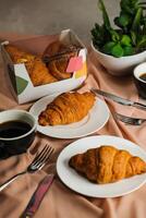 llanura cuerno servido en de madera tablero con taza de negro café aislado en servilleta con cuchillo y tenedor lado ver de francés desayuno horneado comida articulo en gris antecedentes foto