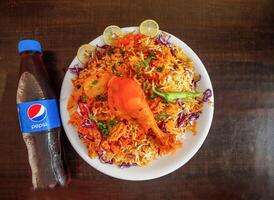 Spicy chicken biryani with potato, pepsi bottle 345 ml, onion and lemon slice served in plate isolated wooden background top view indian spices and pakistani food photo