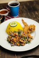 Hot Lemony Chicken Rice Meal served in plate with sauce, cold drink, spoon and fork isolated on wooden board side view of thai food photo