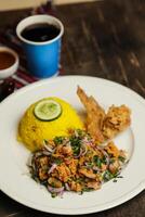 Hot Lemony Chicken Rice Meal served in plate with sauce, cold drink, spoon and fork isolated on wooden board side view of thai food photo