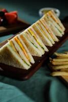 Assorted Club Sandwich isolated on wooden with mayonnaise dip and french fries bucket board side view of italian fast food on background photo