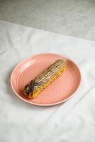 Original Eclair served in plate isolated on napkin side view of cafe baked food on background photo