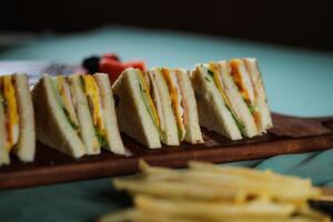 Assorted Club Sandwich isolated on wooden with mayonnaise dip and french fries bucket board side view of italian fast food on background photo