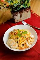 Tropical Pasta Salad With Mix Meat olive with shrimp and prawn served in bowl with flowers and fork isolated on red napkin side view of healthy green food on table photo