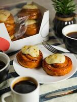 Cinnamon Roll served in plate with cup of black coffee with knife and fork isolated on napkin side view of french breakfast baked food item photo