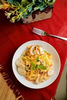 Tropical Pasta Salad With Mix Meat olive with shrimp and prawn served in bowl with flowers and fork isolated on red napkin top view of healthy green food on table photo