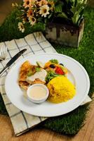 Grilled Jerk Spiced Fillet Fish with rice, dip and salad served in plate with knife and fork isolated on napkin side view of korean style meat food on gassy background photo