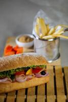 ciabatta ahumado jamón emparedado aislado en de madera con mayonesa inmersión y francés papas fritas Cubeta tablero lado ver de italiano rápido comida en gris antecedentes foto