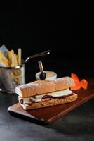 Roasted Beef Sub Sandwich with french fries bucket served on wooden board isolated on dark background side view of breakfast food photo