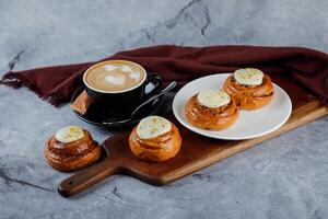Cinnamon Roll served on wooden board with cup of coffee latte art isolated on napkin side view of french breakfast baked food item photo