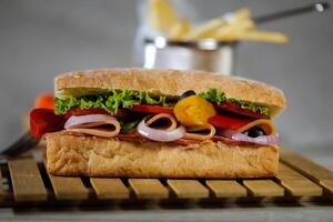 ciabatta ahumado jamón emparedado aislado en de madera con mayonesa inmersión y francés papas fritas Cubeta tablero lado ver de italiano rápido comida en gris antecedentes foto