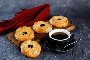 Blueberry Custard Danish served on wooden board with cup of black coffee isolated on napkin side view of french breakfast baked food item on grey background photo