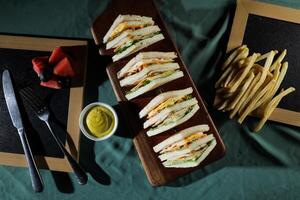 Assorted Club Sandwich isolated on wooden with mayonnaise dip and french fries bucket board top view of italian fast food on background photo