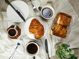 Chocolate Croissant served on plate with cup of black coffee with knife and fork isolated on napkin top view of french breakfast baked food item on grey background photo