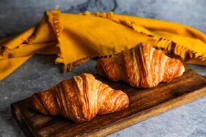Plain Croissant served on wooden board isolated on yellow napkin side view of french breakfast baked food item on grey background photo