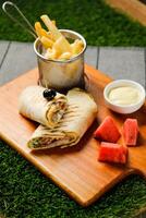 Naga Beef egg wrap roll filled with tomato, onion, cucumber with french fries, mayo and watermelon slice dip served on wooden board top view of fastfood appetizer photo