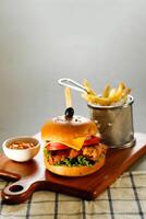 chipotle pollo hamburguesa incluir queso rebanada, tomate, cebolla y lechuga hoja servido en de madera tablero con inmersión y francés papas fritas Cubeta aislado en gris antecedentes lado ver de aperitivo rápido comida foto