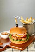 picante naga carne de vaca hamburguesa incluir queso rebanada, tomate, cebolla y lechuga hoja servido en de madera tablero con inmersión y francés papas fritas Cubeta aislado en gris antecedentes lado ver de aperitivo rápido comida foto